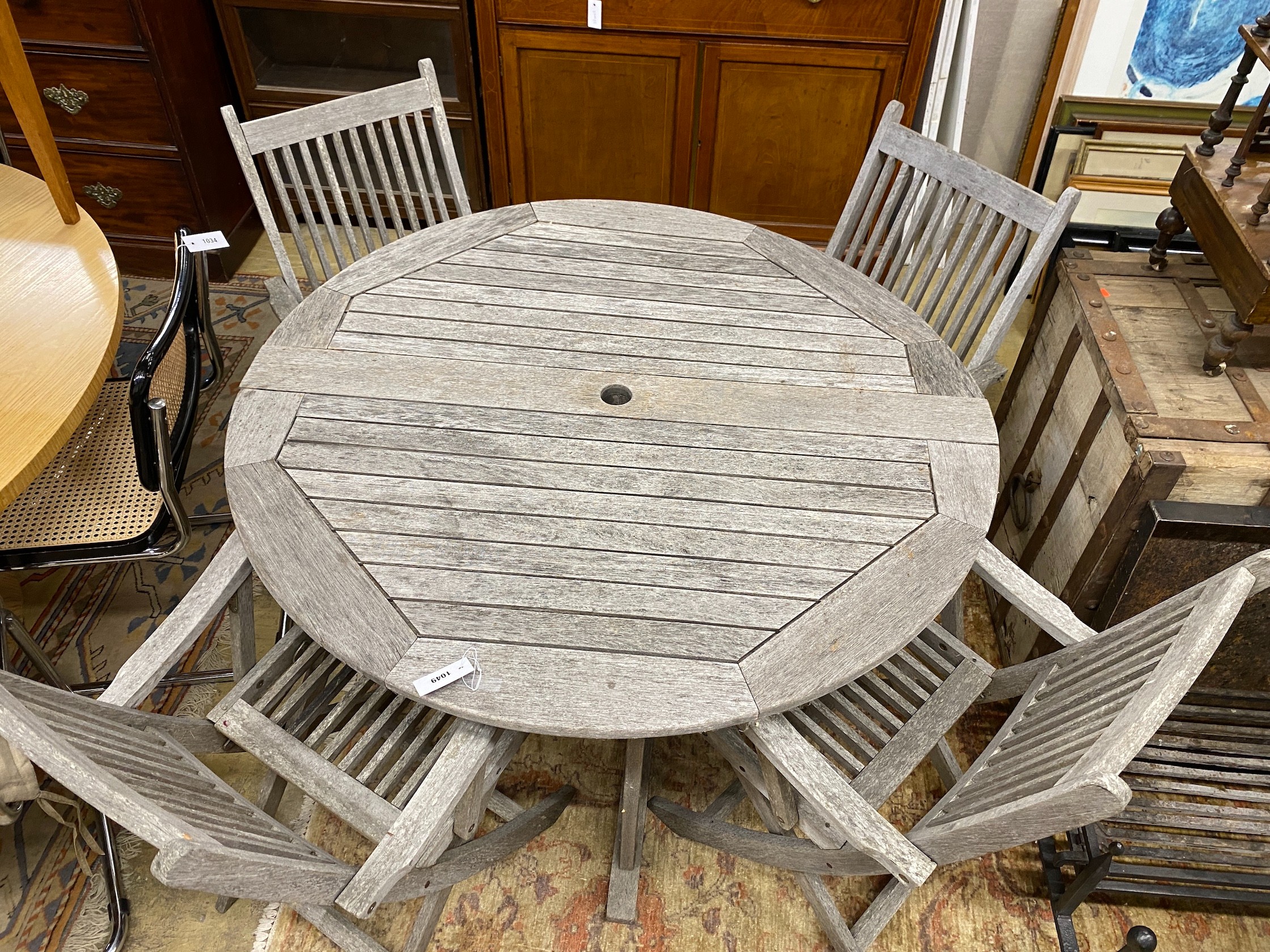 A circular weathered teak folding garden table, diameter 120cm, height 74cm, together with four teak folding elbow chairs